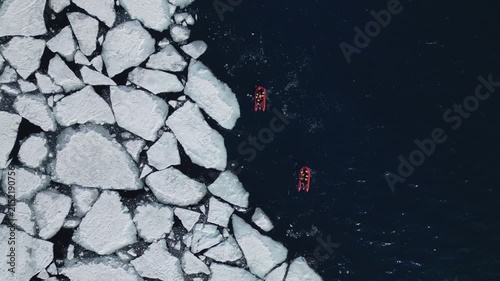 Aerial top-down view of red Zodiac boats navigating through melting sea ice in Svalbard during arctic summer