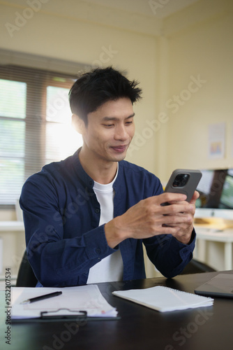 Young Asian businessman using a smartphone while working at his office desk.