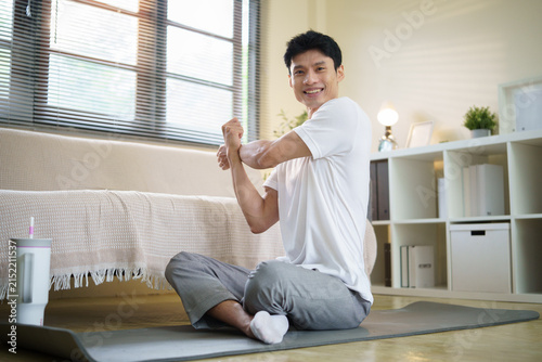 Cuadro en lienzo Young Asian man stretching his upper body during a home workout routine