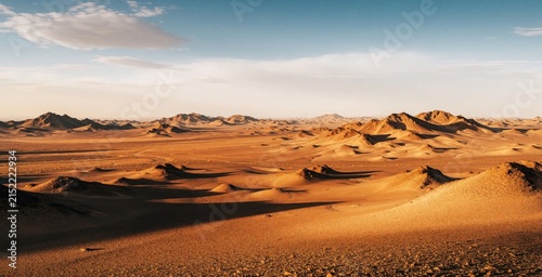 Vast desert landscape with sand dunes, mountains under blue sky. Arid terrain shows endless hills, dry ground in China. Scenic view of Gobi Desert wilderness during sunny day. Beautiful nature