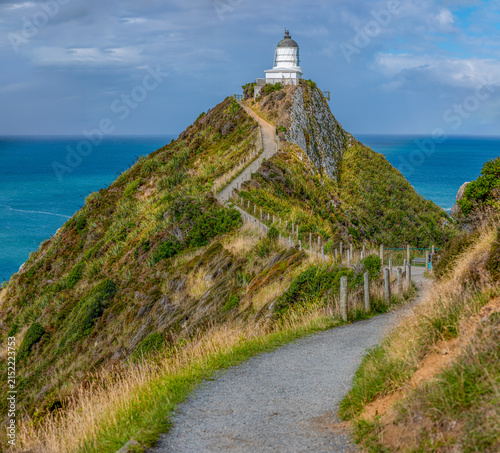Nugget Point Lighthouse auf schmalem Felsgrat mit Blick auf die Nuggets-Felsen und schwachem Regenbogen, Otago, Neuseeland
