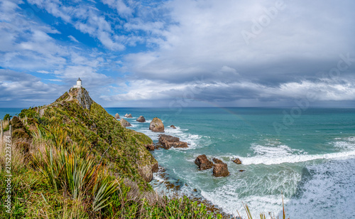 Nugget Point Lighthouse auf schmalem Felsgrat mit Blick auf die Nuggets-Felsen und schwachem Regenbogen, Otago, Neuseeland