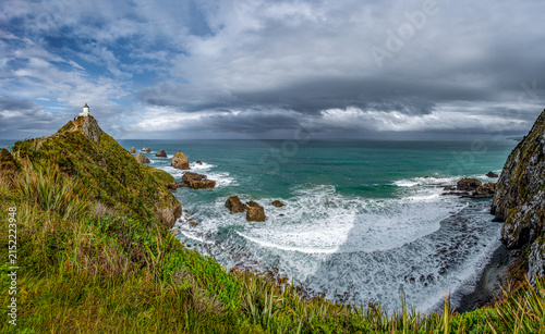 Nugget Point Lighthouse auf schmalem Felsgrat mit Blick auf die Nuggets-Felsen und schwachem Regenbogen, Otago, Neuseeland