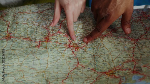 Two pairs of hands (a man's and a woman's) are pointing to and tracing a location on a paper road map (focusing on the Hannover area and its surroundings in Germany).