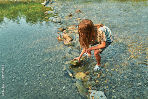Boy crouching at the edge of a shallow river stacking rocks