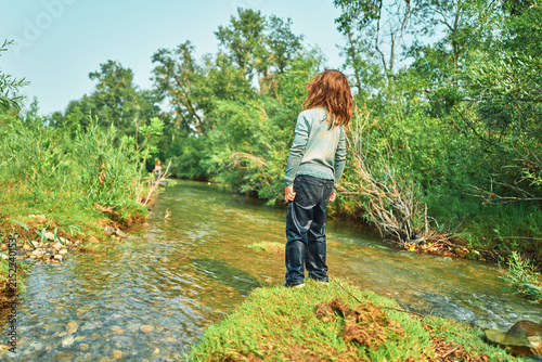 Boy standing on a grassy riverbank looking downstream