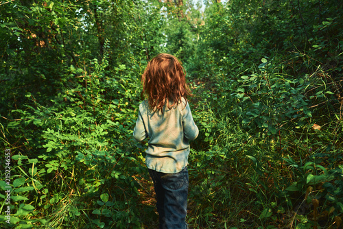 Boy walking into dense green bushes from behind