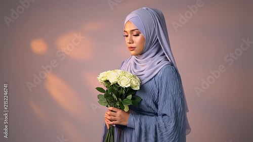 A serene portrait of a modestly dressed Muslim woman in a lilac hijab holding a white bouquet against a warm bokeh background