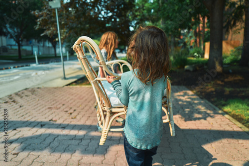 Two boys carrying a rattan loveseat along a brick sidewalk