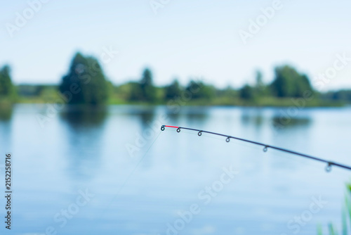 Картината върху платно Fishing feeder rod tip over calm lake water with blurred natural landscape background