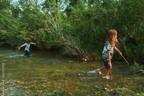 Two boys wading through a river with sticks