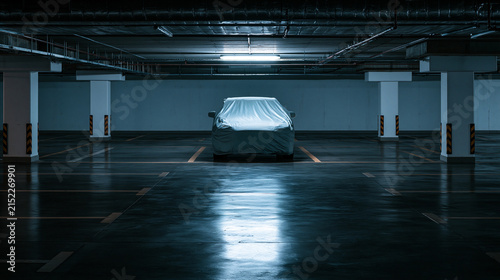 A dark atmospheric underground parking garage with glossy black concrete flooring and empty marked parking bays, a single car fully covered