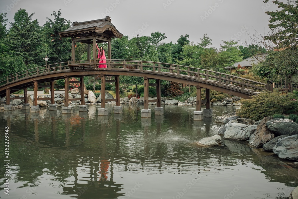 Fototapeta premium A beautiful young girl in a bright pink costume in a Japanese garden. The time of the year is summer.