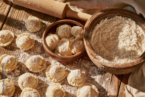 Fresh homemade dumplings and dough on a rustic table with flour, bowls and a rolling pin, cozy country kitchen scene, traditional food and home bakes.