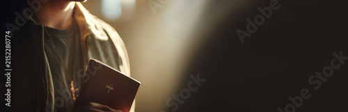 Man standing with bible in hand under light ray in dark church. Religious faith and spiritual devotion concept. Holy belief, prayer time and worship experience in sacred building.