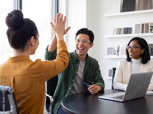 Enthusiastic multiethnic business colleagues high-fiving in a contemporary office setting, celebrating success.