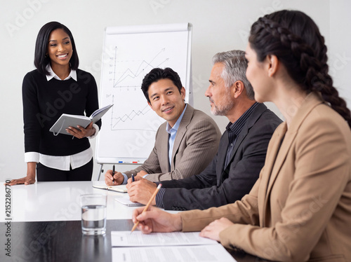 Confident young black businesswoman presenting ideas to diverse colleagues during a corporate meeting with charts.