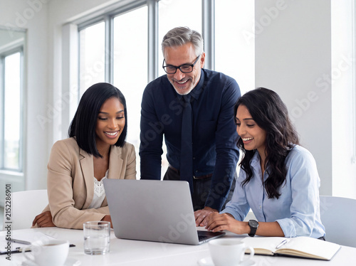 Diverse business team collaborating on a laptop in a bright modern office, showcasing teamwork and success.