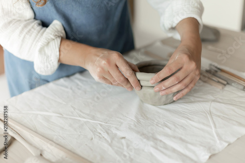 Woman potter meticulously shaping clay in a studio setting, demonstrating a creative and focused approach, captured in a close-up side view, the scene showcases.