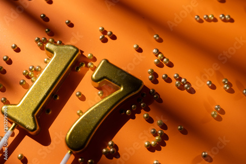 Fotografie vibrant festive backdrop for 17th birthday, made of gold candles shaped like number seventeen, placed on an orange background with sprinkles