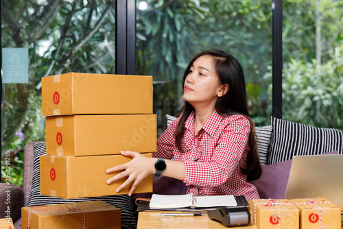 Female small business owner lifting parcel boxes in home office. Female ecommerce entrepreneur processing online shopping orders. Work from home online seller managing shipping and delivery concept.