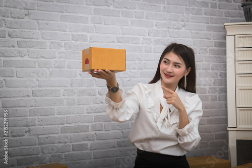 Smiling female online seller showing small shipping box in office. Small business owner packaging product for customer delivery. Ecommerce business and online delivery concept.