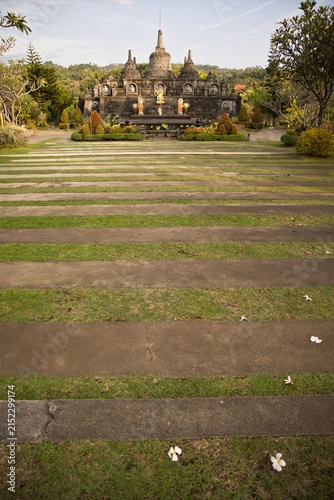 Fotografie Magnificent mini replica of Borobudur temple surrounded by lush gardens, pathways, and golden Buddha statues under a blue sky at Brahma Vihara Arama monastery in Bali