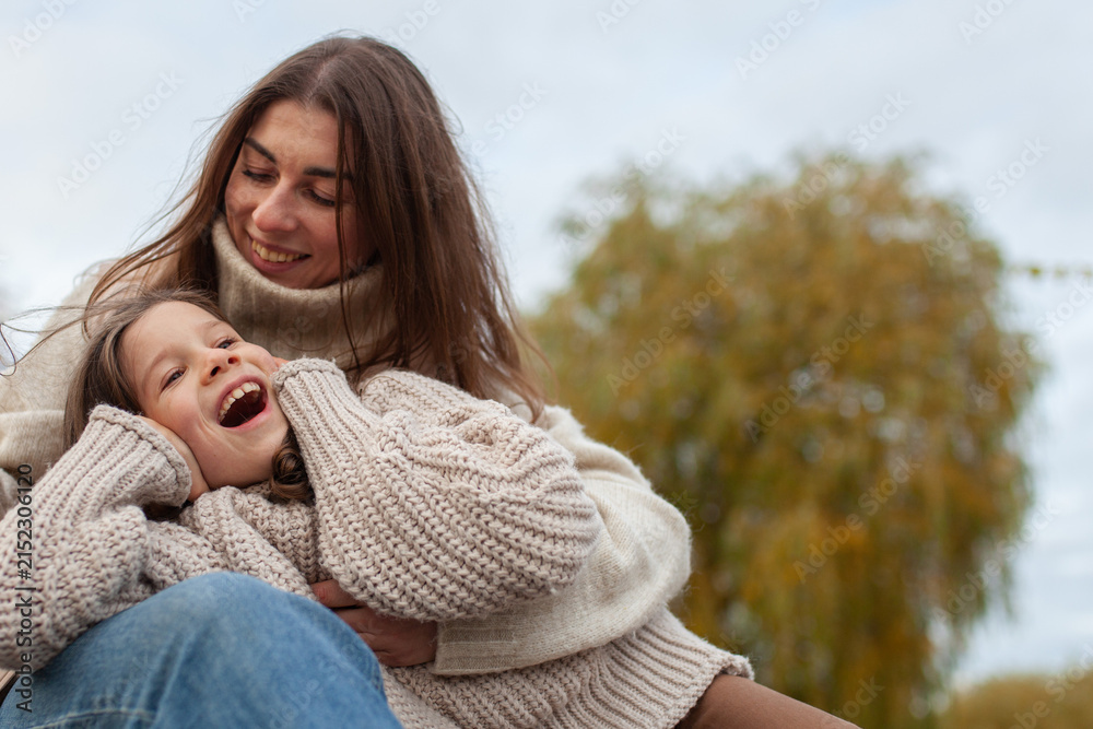 Fototapeta premium Happy mother and daughter laughing together outdoors in autumn, wearing cozy knit sweaters. Unconditional love, warmth, and joy in family relationships. Mother's day.