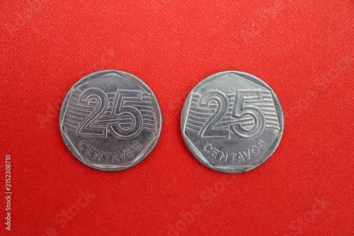 An old 1990s stainless steel 25 centavos Brazilian coin with a heptagonal inner shape, on red background.