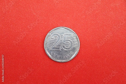 An old 1990s stainless steel 25 centavos Brazilian coin with a heptagonal inner shape, on red background.