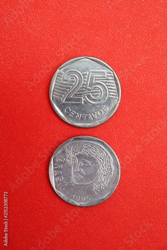 An old 1990s stainless steel 25 centavos Brazilian coin with a heptagonal inner shape, on red background.