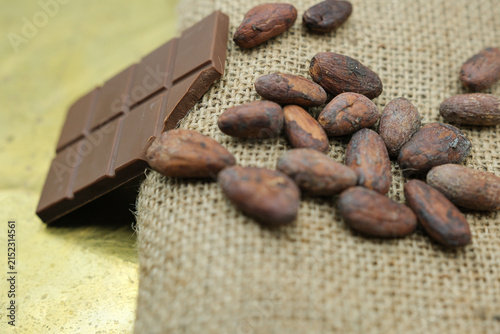 Cocoa Beans on Jute Sack with Chocolate Bar. Golden Background. Cocoa Bean Value. Shallow Depth of Field.