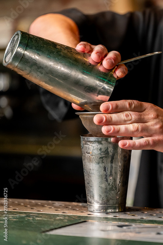 Fotografie A bartender's hands double straining a cocktail from a metal shaker tin through