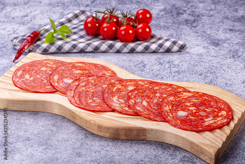 Obraz na płótnie Sliced chorizo salami on wooden board with cherry tomatoes and chili pepper