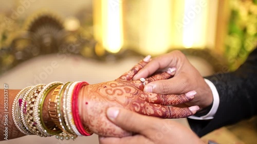 Groom putting engagement ring on bride hand with henna design at Indian wedding ceremony