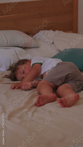 Obraz na płótnie Toddler sleeping peacefully on bed at home, briefly brushing away fly while rema