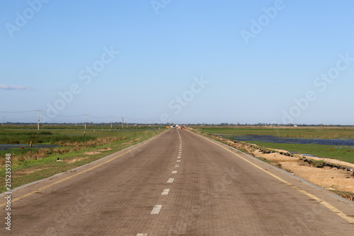 Scenic rural wetland and agricultural landscapes featuring shallow floodwater, green grasslands, open fields, dirt roads, palm trees and expansive blue skies. The images capture peaceful countryside