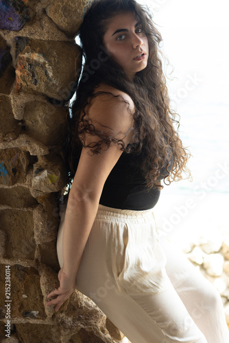Young woman posing by stone wall looking at camera