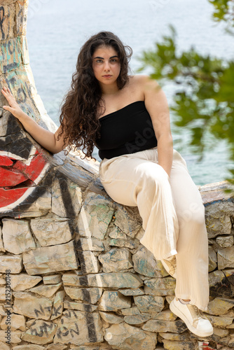 Young woman sitting on graffiti stone wall by sea