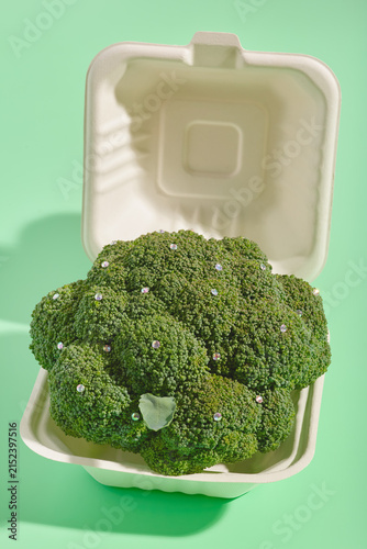 Sustainable takeout container holding decorated broccoli on green