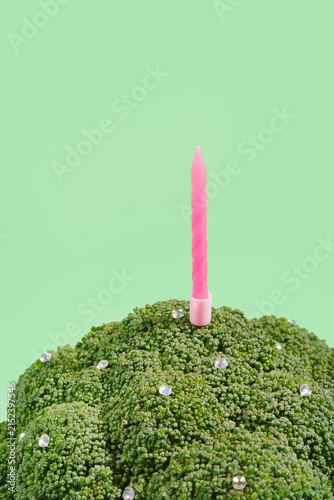 Pink birthday candle standing in broccoli against green background