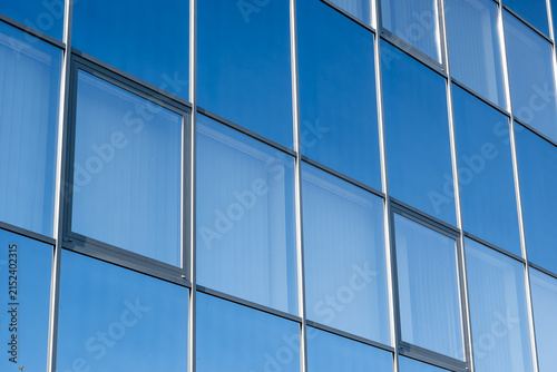 Картината върху платно Modern office building facade with blue glass windows reflecting the clear sky,