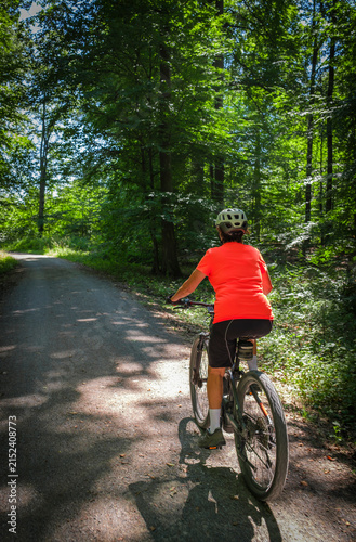 Canvas Print female Cyclist riding a bicycle along a peaceful forest avenue surrounded by lush green trees and dappled sunlight