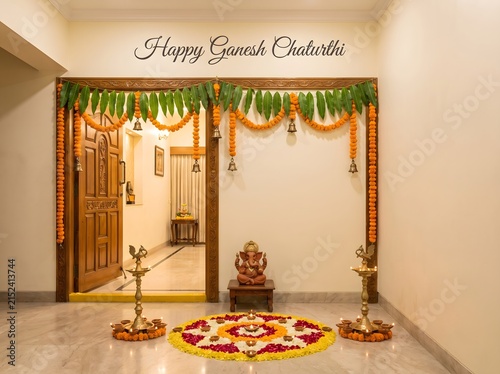 Lord Ganesha idol sits on wooden pedestal with floral rangoli design.