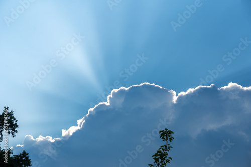 The sun is shining from behind the cloud in the  sky.