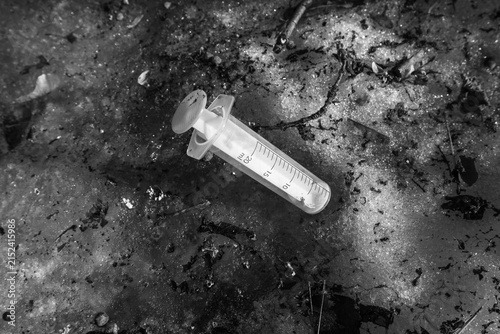 Used plastic medical syringe lying in dirty melting snow close up