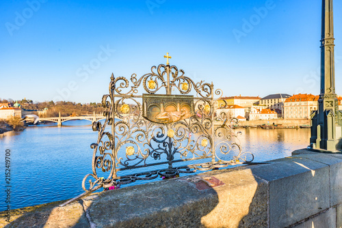 Relief plaque of St John of Nepomuk on Charles Bridge railing over Vltava River in Prague, UNESCO World Heritage Site, on sunny day