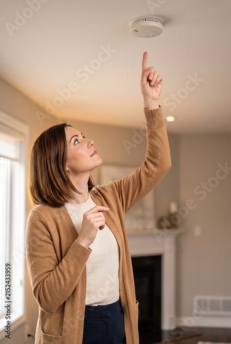 Woman performing a safety check by pressing the button on a ceiling-mounted smoke alarm