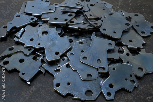 Pile of small grey metal brackets with multiple holes used for joining and connecting construction materials in industrial settings.