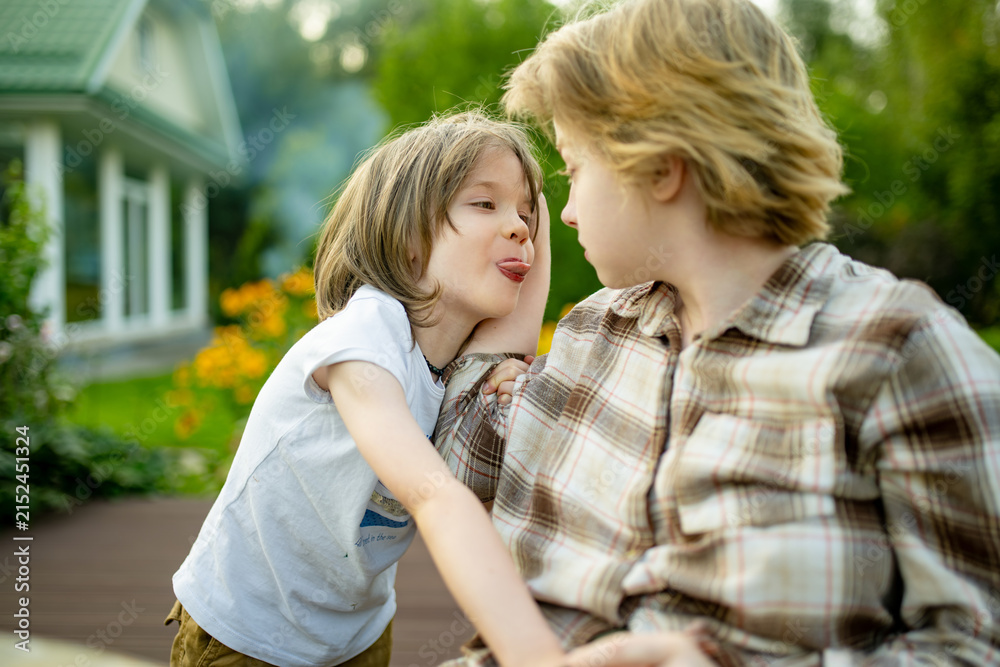 Fototapeta premium Playful young boy teasing his older sister outdoors in the garden. Funny candid moment of sibling interaction and playful family relationship.